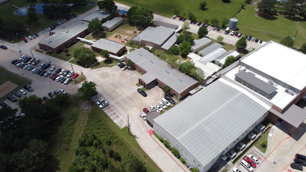 Aerial view of a large school campus with parking lot and surrounding greenery - FMF Roofing